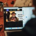 An image showing a laptop screen over a person's shoulder, with an Indigenous Australian on the screen.